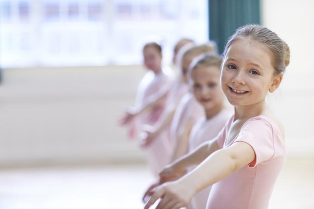 Gruppe junger Balletttänzerinnen in rosa Kostümen, die sich lächelnd im Tanzsaal aufstellen.