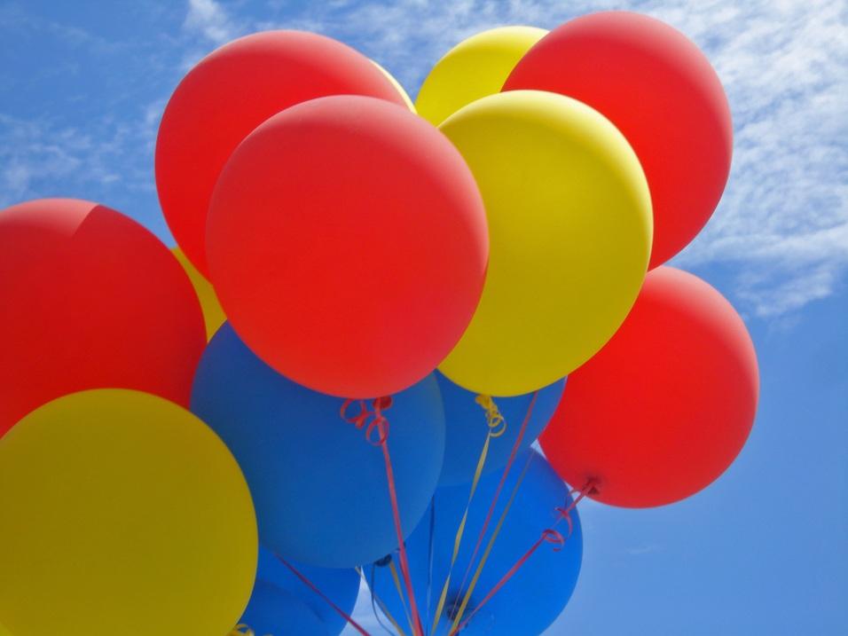 Bunte Luftballons in Rot, Gelb und Blau unter einem strahlend blauen Himmel mit wenigen Wolken.