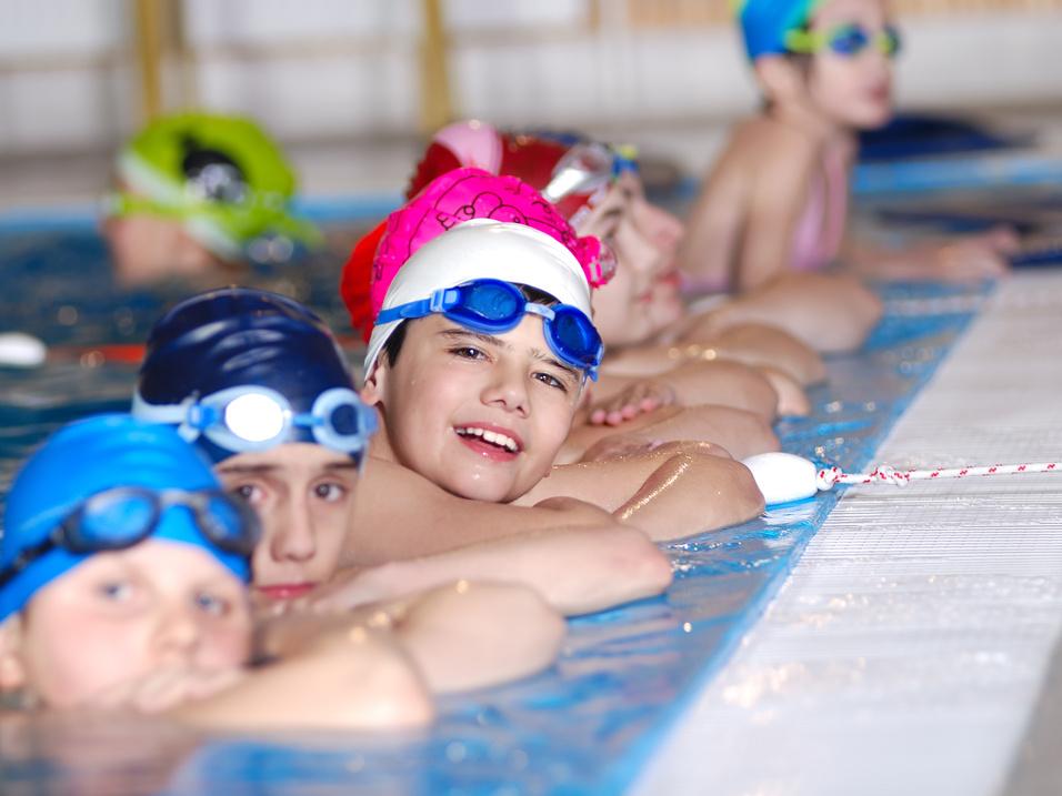 Gruppe von Kindern in Schwimmbekleidung, die an einem Schwimmbeckenrand entspannen und lächeln.