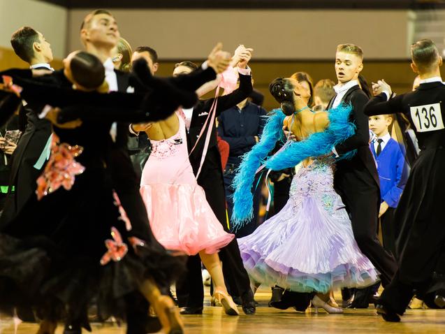 Tanzpaare in eleganten Kostümen tanzen auf einem Parkettboden bei einem Tanzwettbewerb.